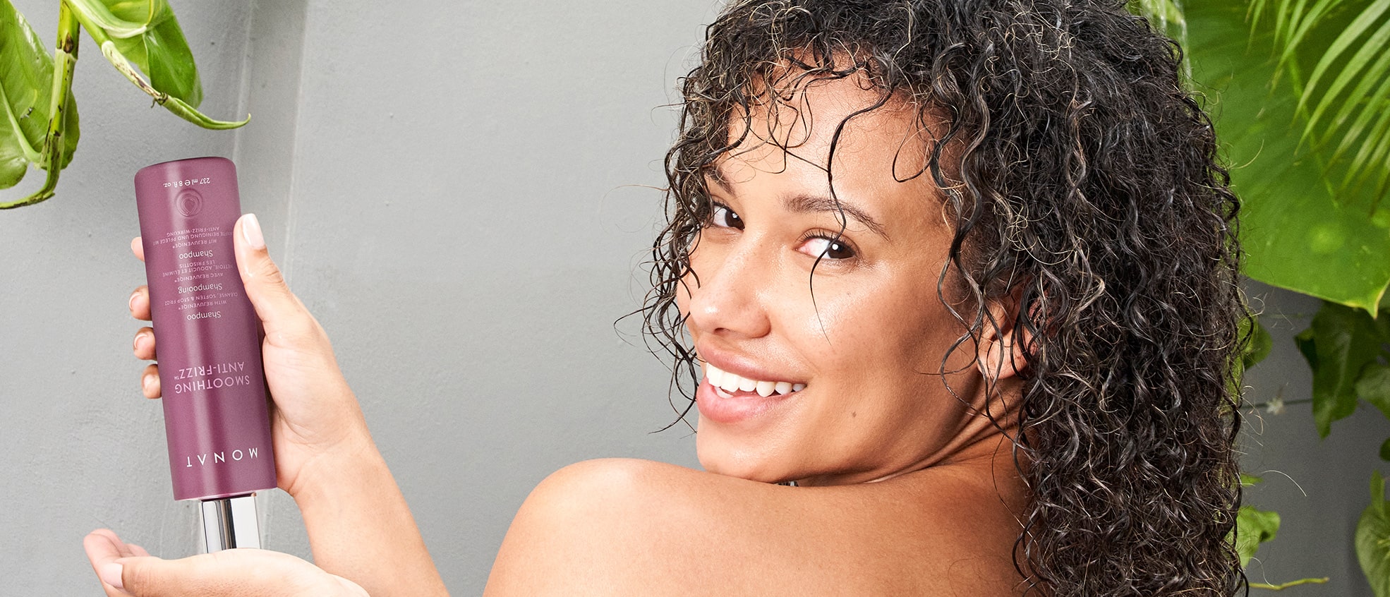 A brunette woman with curly hair holding Smoothing Anti-Frizz™ Shampoo.