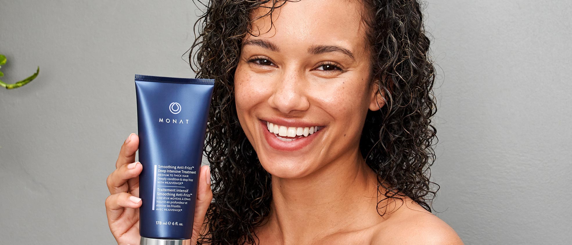Brunette woman with curly hair smiling while holding Smoothing Anti-Frizz™ Deep Intensive Treatment.