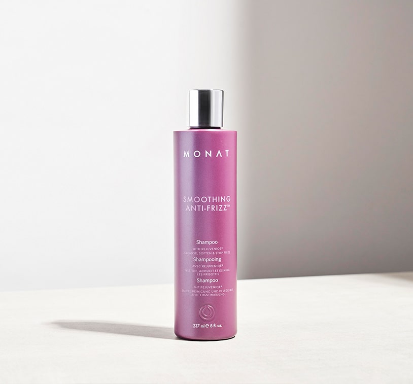 Smoothing Anti-Frizz™ Shampoo laying on a tan surface, next to greenery and leaves.