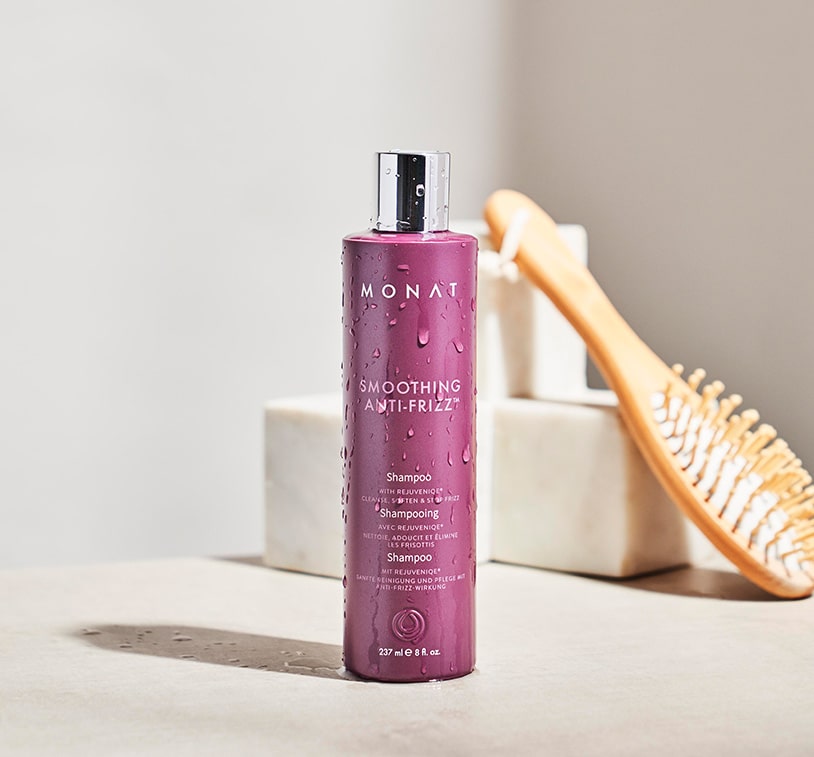 Smoothing Anti-Frizz™ Shampoo laying on a ceramic plate, next to drops of REJUVENIQE® and Smoothing Anti-Frizz™ Shampoo.