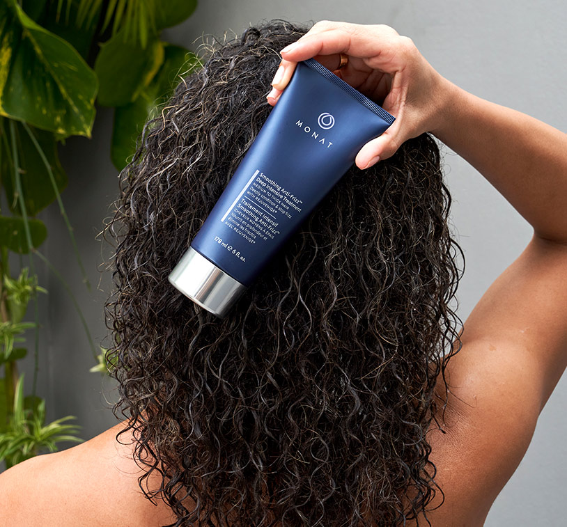 A brunette woman with curly hair holding Smoothing Anti-Frizz™ Deep Intensive Treatment.