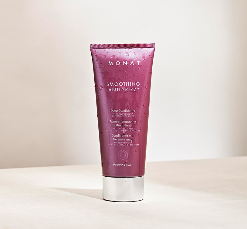Smoothing Anti-Frizz™ Deep Conditioner laying on a tan surface, next to different ingredients.