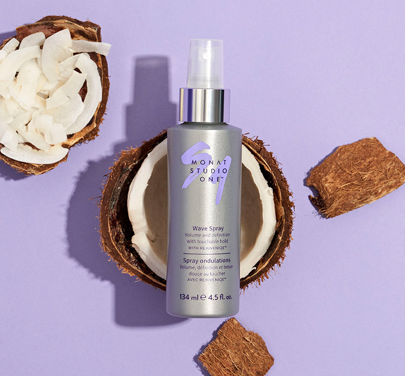 MONAT STUDIO ONE™ Wave Spray laying on top of an open coconut, next to coconut pieces, while sitting on a purple background. 