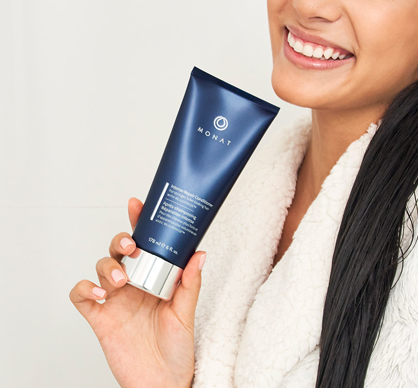 MONAT’s Damage Repair Shampoo being upheld by a woman’s hand, showcasing the product’s aesthetics. Subject 
		is placed in front of a peach color background.