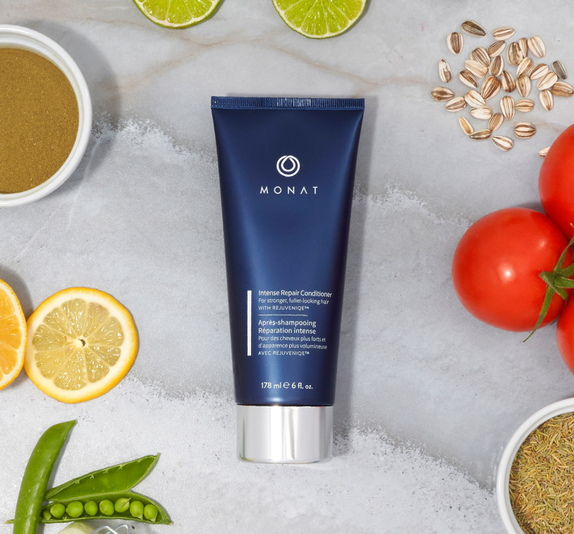 MONAT’s Damage Repair Shampoo stands over a white solid background setting displaying raw ingredients such as oils, citrus & 
				herbs along with additional glass ornaments around it.