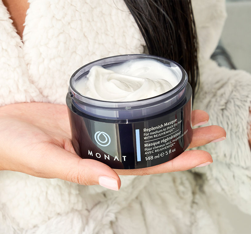 A female hand holding an open container of the Replenish Masque.