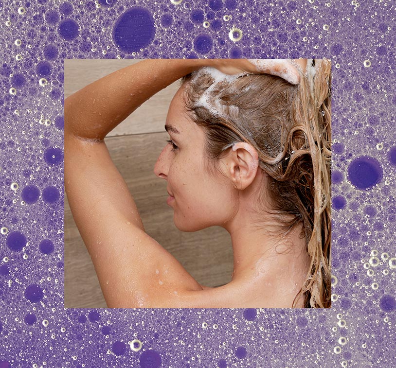 A blonde female washing her hair in the shower, overlaying a photo of bubbles on a purple background.