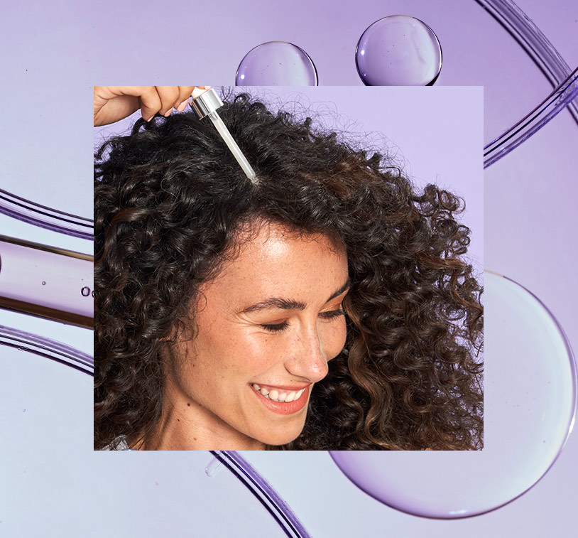 Brunette female smiling while applying IR Clinical™ Hair Thinning Defense to her curly hair, overlaying a photo of bubbles on a purple surface.
