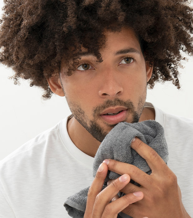 Afroamerican male drying his face with gray towel.