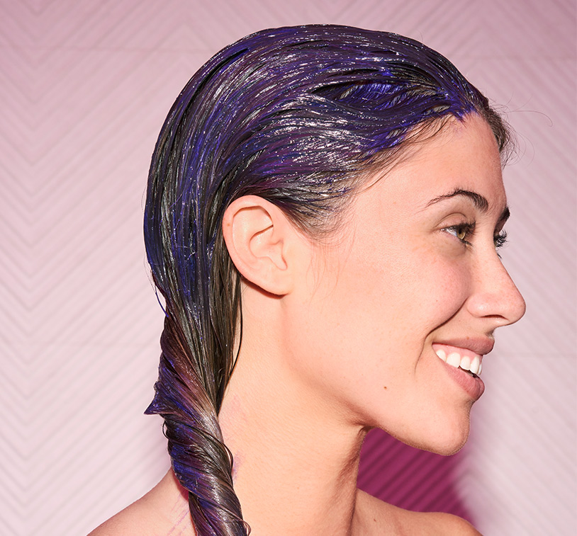 Closeup of a woman’s brunette hair being combed. Depicts smooth results. Subject poses in front of a solid, 
			lavender color background.