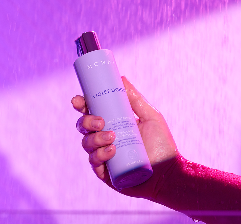Brunette female washing her hair in the shower with Violet Lights™ Anti-Brass Shampoo, while overlaying a texture shot of Violet Lights™ Anti-Brass Shampoo.