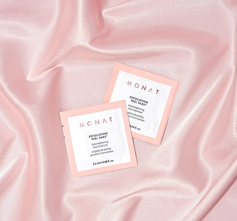 two MONAT exfoliating peel pads sachets over a pink satin fabric