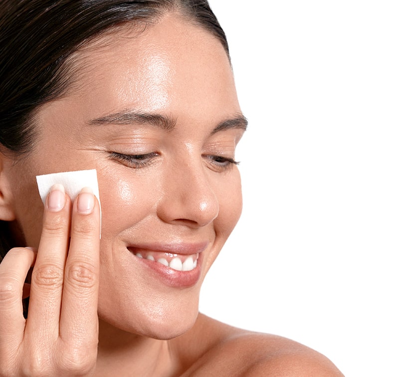 female using monat exfoliating peel pads on her cheek on top of cucumber slices into submerged in water background