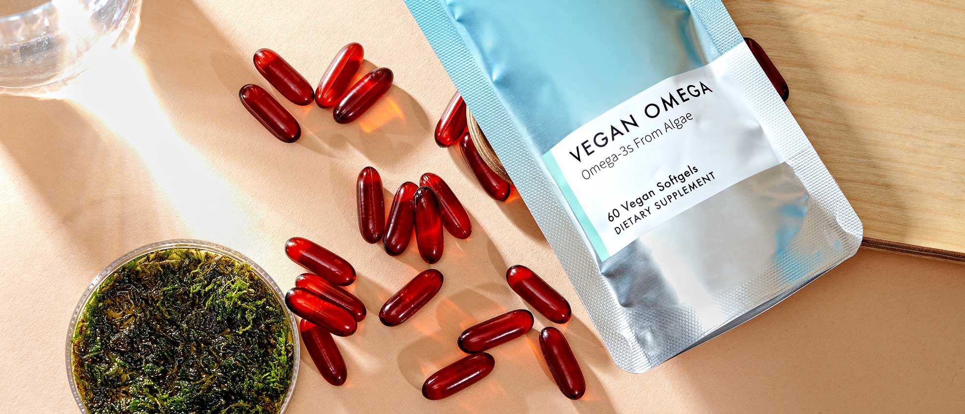 picture of vegan omega sachet next to red soft gels and petri dish marine algae. 