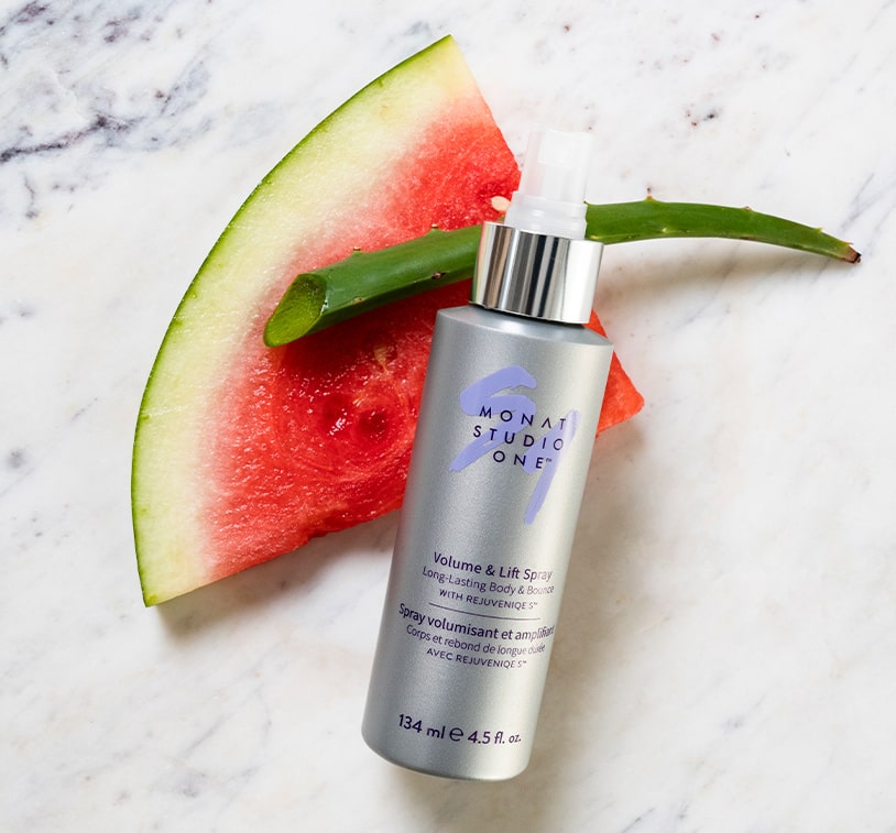 MONAT STUDIO ONE™ Volume & Lift Spray on a marble surface, next to a watermelon slice and aloe vera.