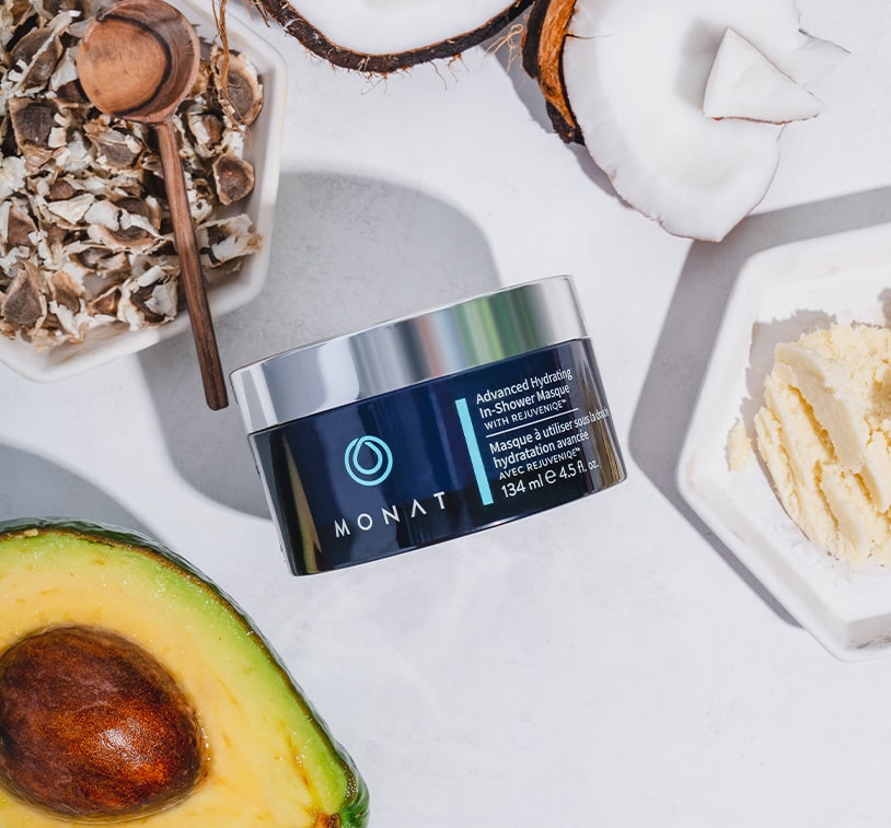 Advanced Hydrating In-Shower Masque on a flat surface next to coconut pieces, avocado and other ingredients.