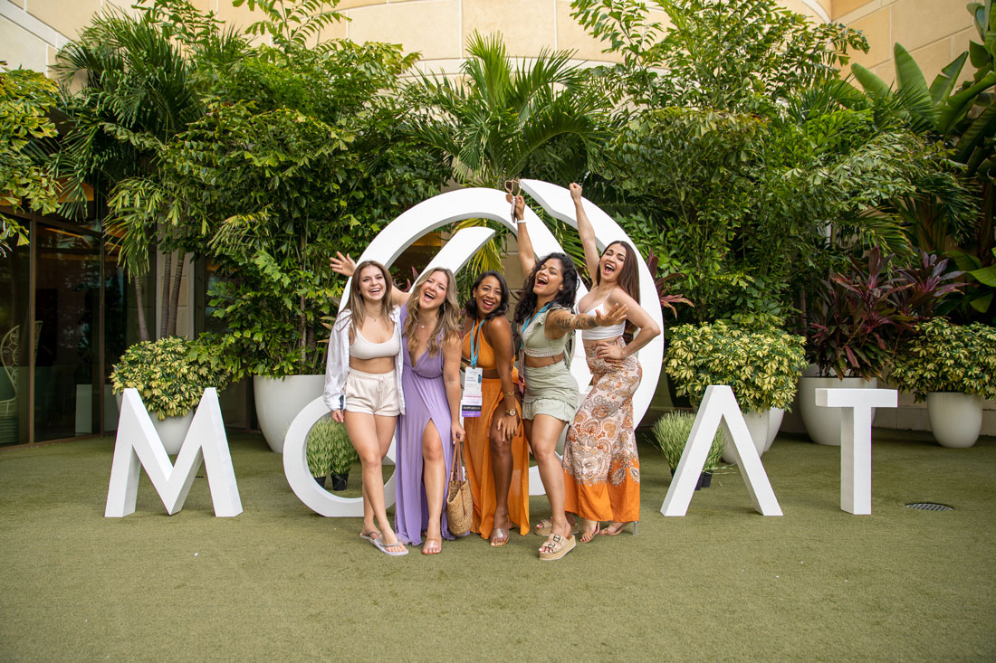 group of women posing with a Monat logo in the background