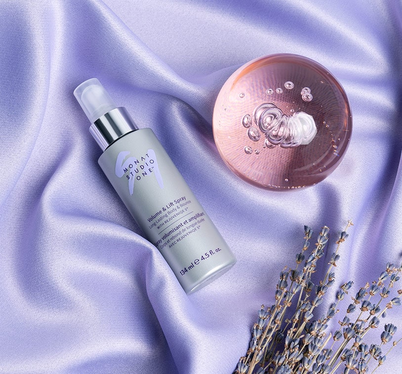 MONAT STUDIO ONE™ Volume & Lift Spray laying on a purple silk blanket, next to a lavender plant and glass sphere.