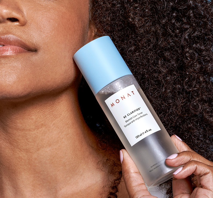 A brunette female with curly hair holding BE CLARIFIED™ Blemish Care Toner against her face.