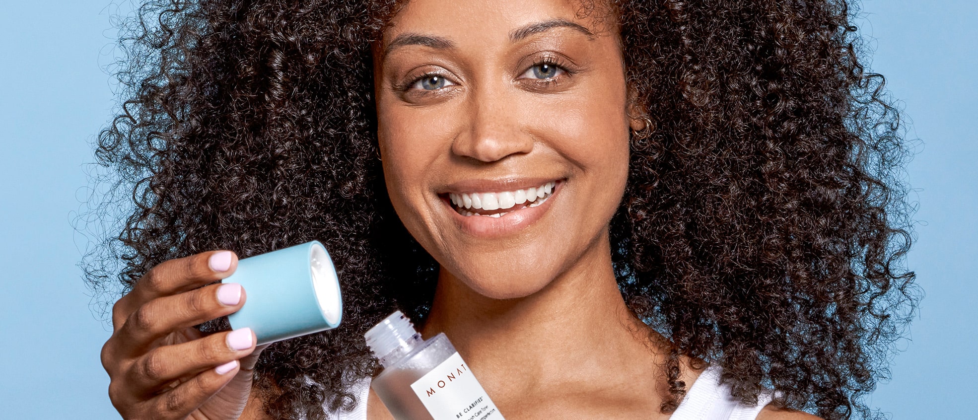 A brunette female with curly hair smiling while opening  BE CLARIFIED™ Blemish Care Toner.