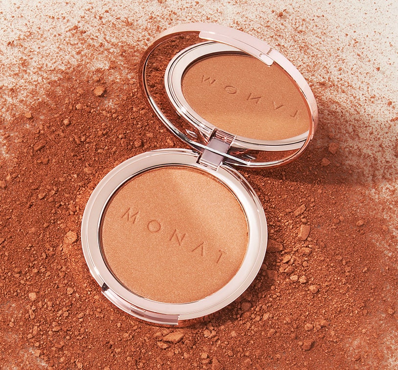 MONAT Radiant Bronzer™ on a solid surface, on top of pieces of golden bronzer powder. 
