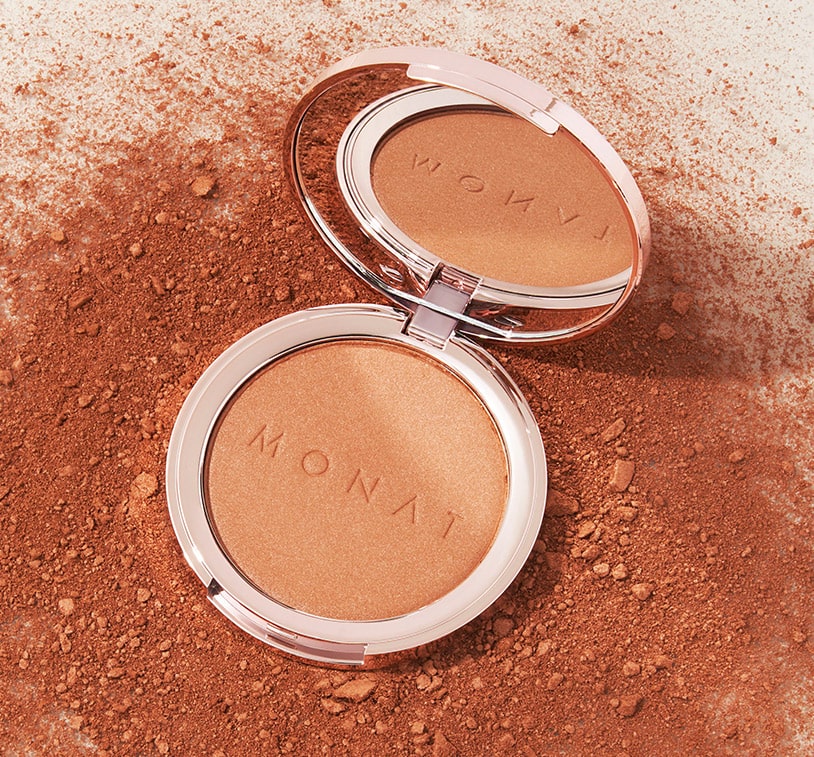 MONAT Radiant Bronzer™ on a solid surface, on top of pieces of golden bronzer powder.