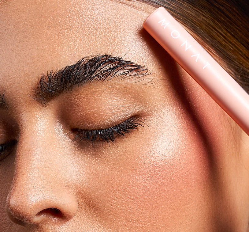 Female holding the brush of the MONAT IR Clinical™ Clear Brow Gel infront of her brows.