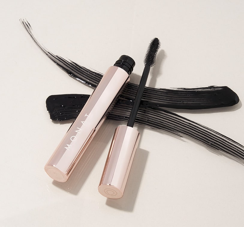 MONAT IR Clinical™ Mascara Jetsetter Black on a flat surface, with streaks of black mascara.