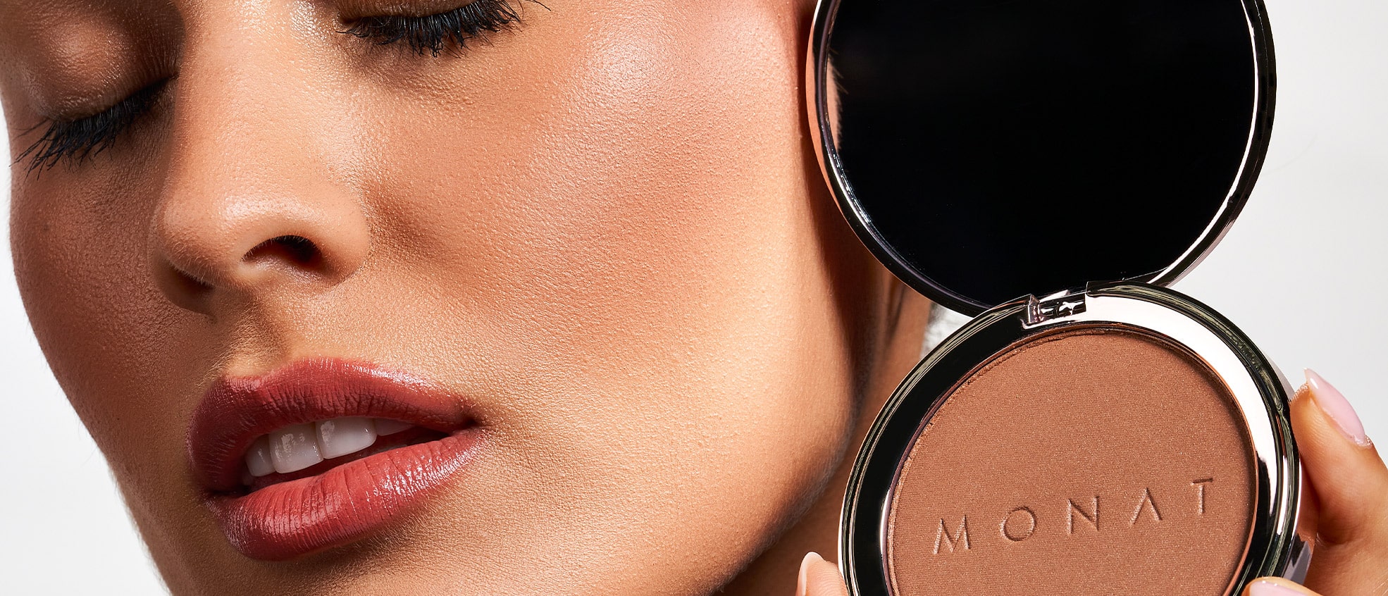 Female holding the MONAT Radiant Bronzer™ next to her face.
