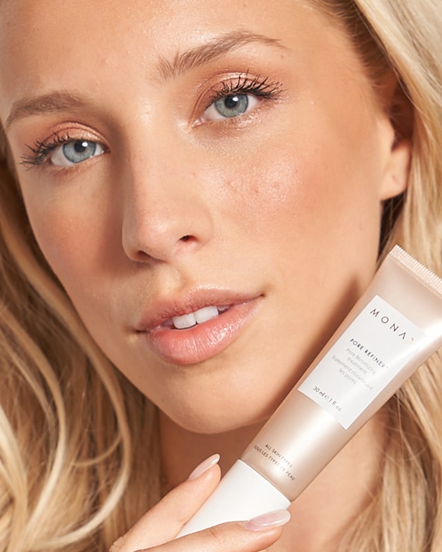 a close up picture of a blond female's face holding a Monat pore refiner tube next to her chin