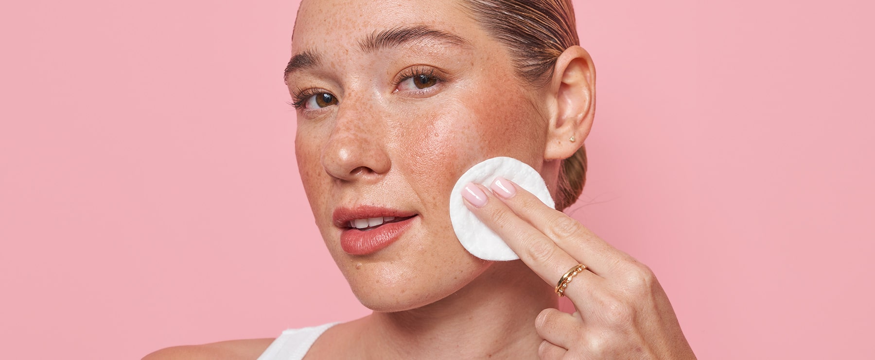 Smiling woman with clean skin using MONAT Micellar Water with a cotton pad on her face.