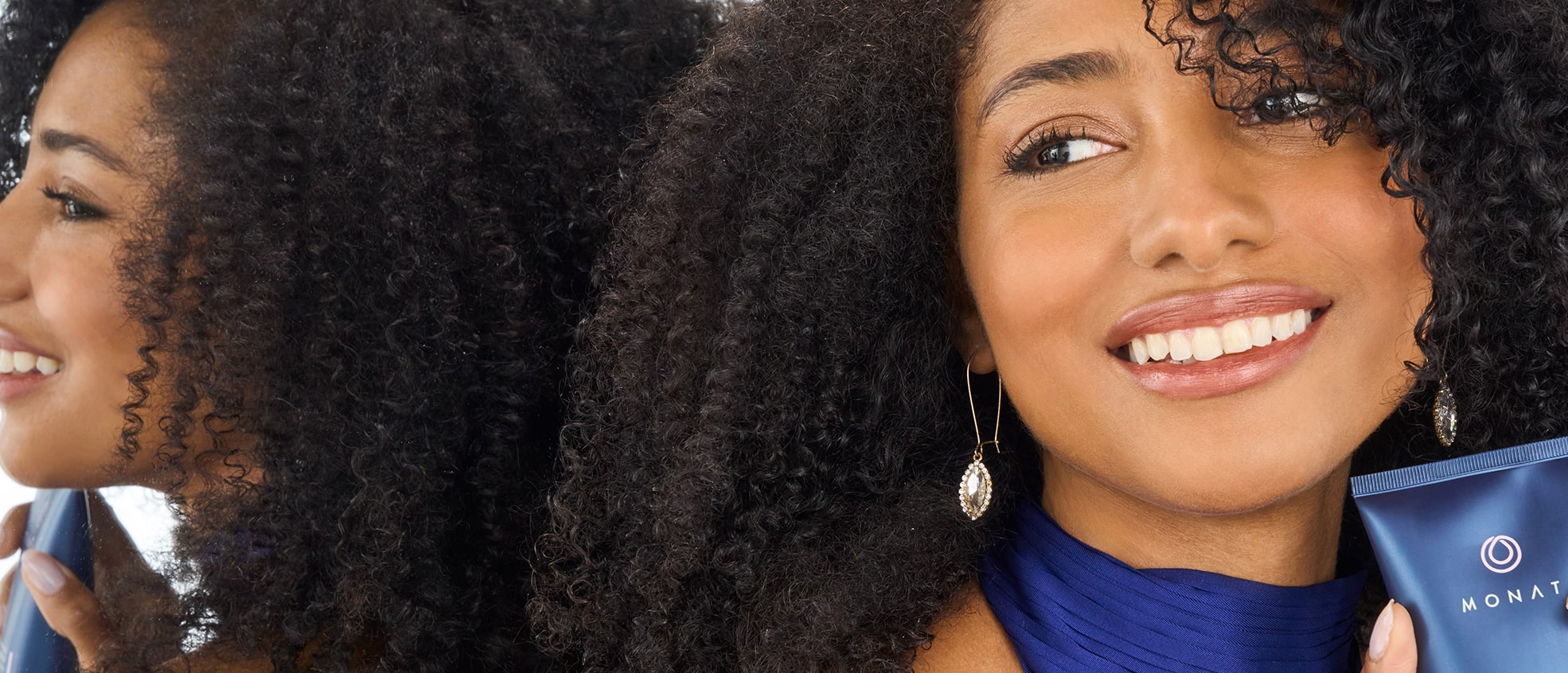 Smiling woman with curly hair holding a tube of MONAT Curl Perfection™ Curl Defining Cream.