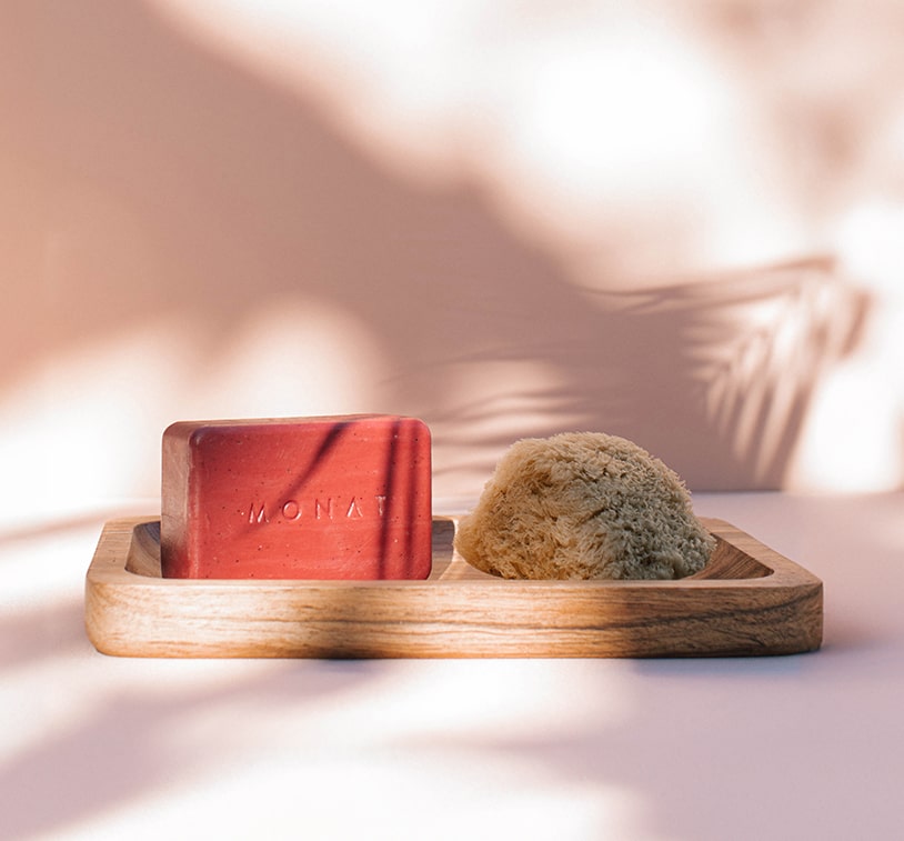MONAT body bar next to a natural sponge on a wooden soap dish.