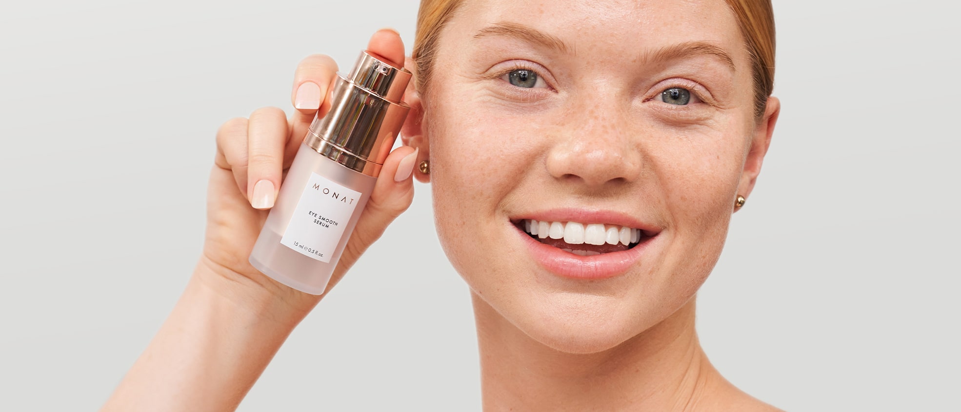 Smiling woman holding MONAT Eye Smooth™ Serum next to her face.