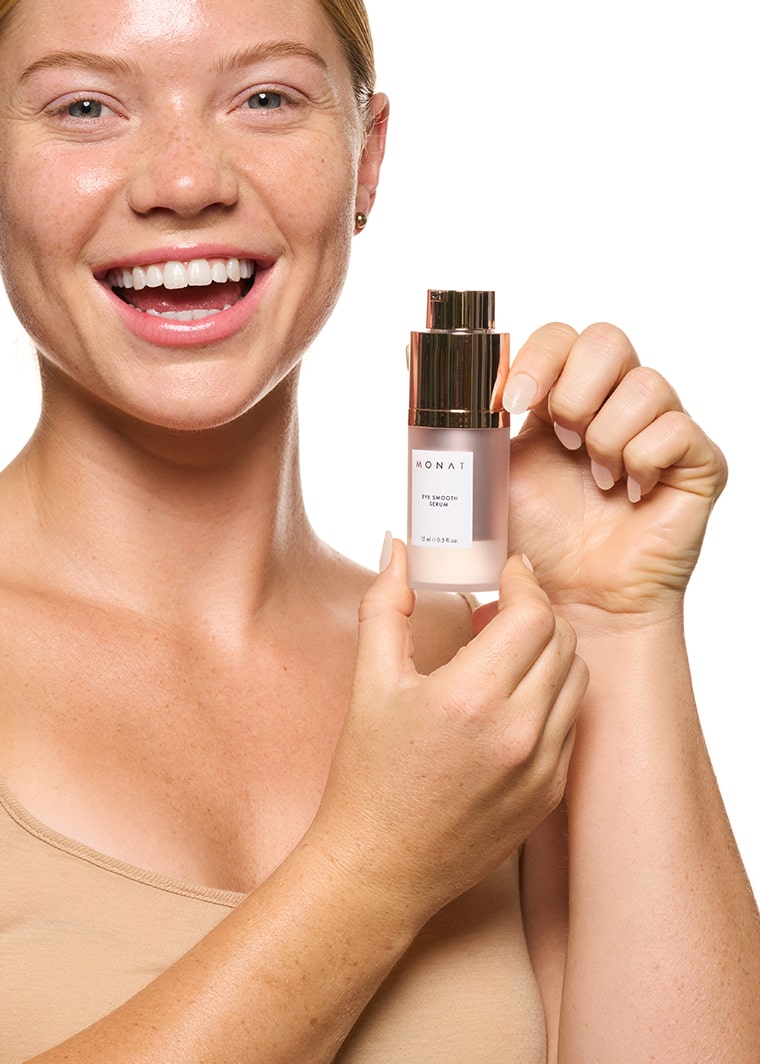 Smiling woman holding MONAT Eye Smooth™ Serum next to her face.