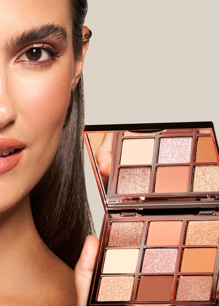 Close-up of a model's face with a subtle makeup look holding a MONAT Glam essentials eye shadow palette