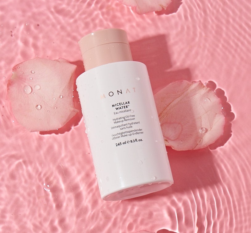 Bottle of MONAT Micellar Water placed on a pink background with water ripples.