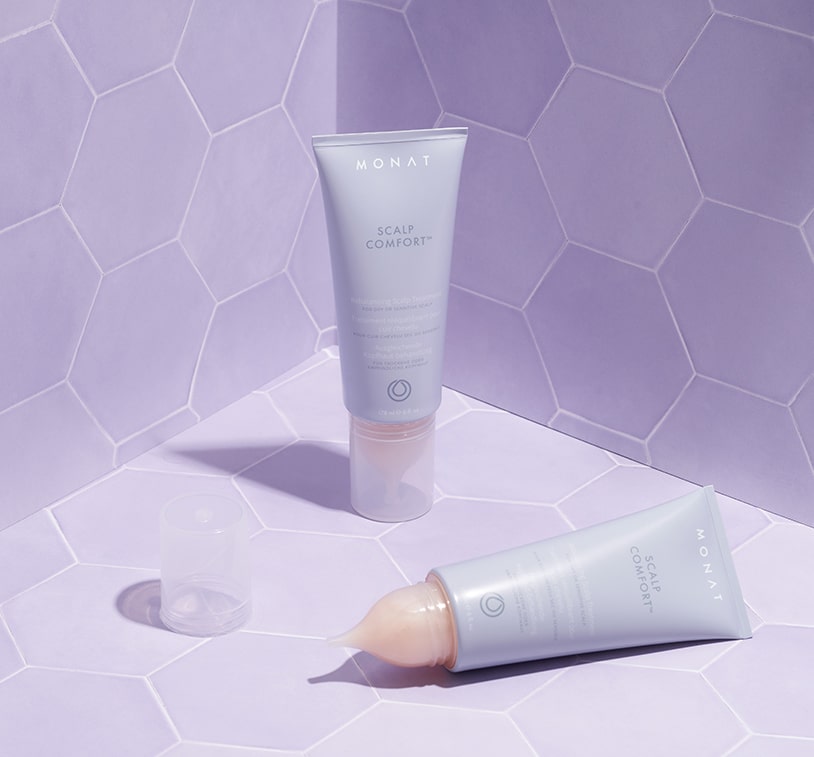 MONAT Scalp Comfort Treatment tube lying on a purple background with the cap off, displaying the nozzle.