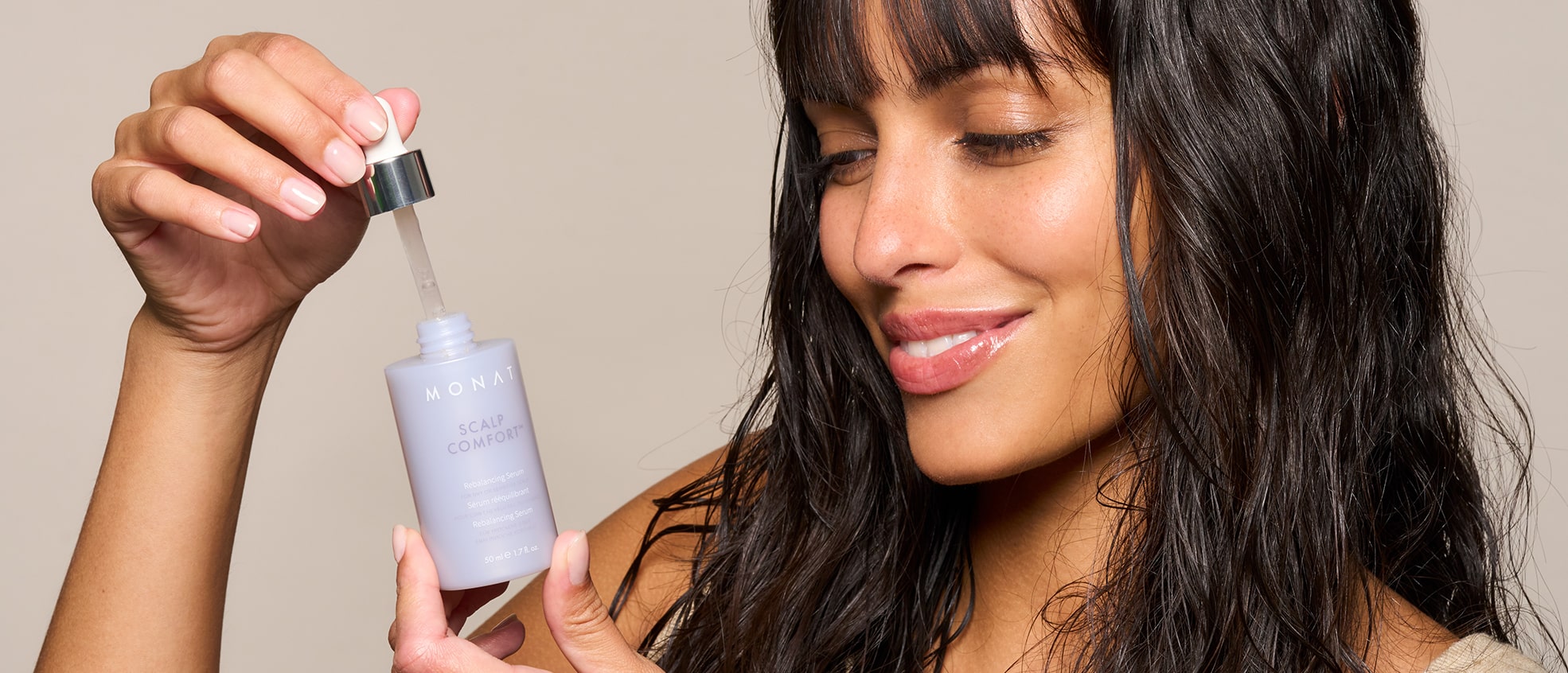 Close-up of a smiling model with dark hair holding the Scalp Comfort Rebalancing Serum dropper