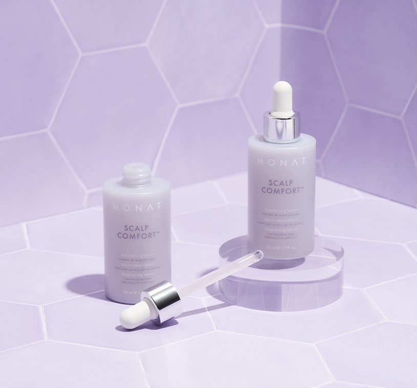 Two Scalp Comfort Rebalancing Serum bottles standing on a purple background with a mirror reflecting one of the bottles.