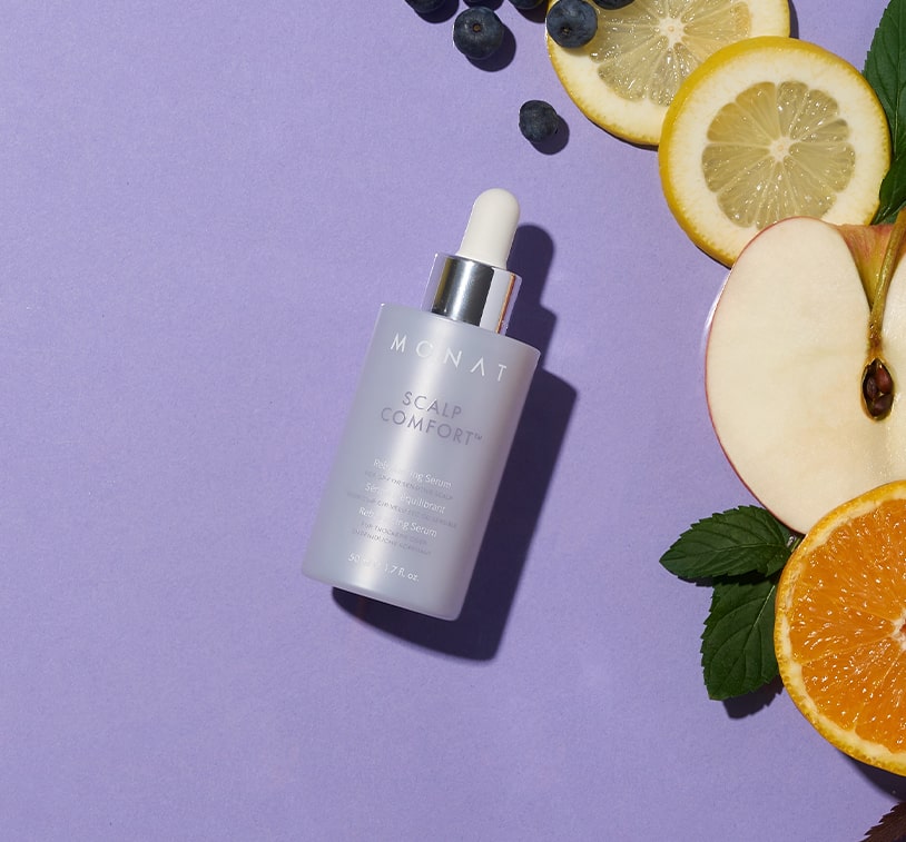 Scalp Comfort Rebalancing Serum bottle lying on a purple surface, surrounded by fresh fruit slices and botanical leaves.