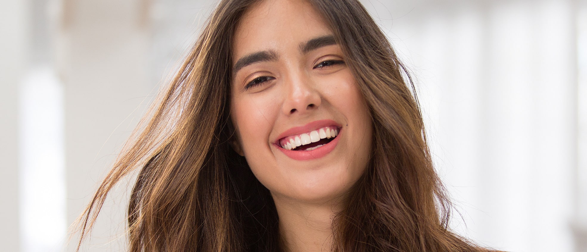 Smiling woman with long brown hair smiling at the camera in a well-lit environment.