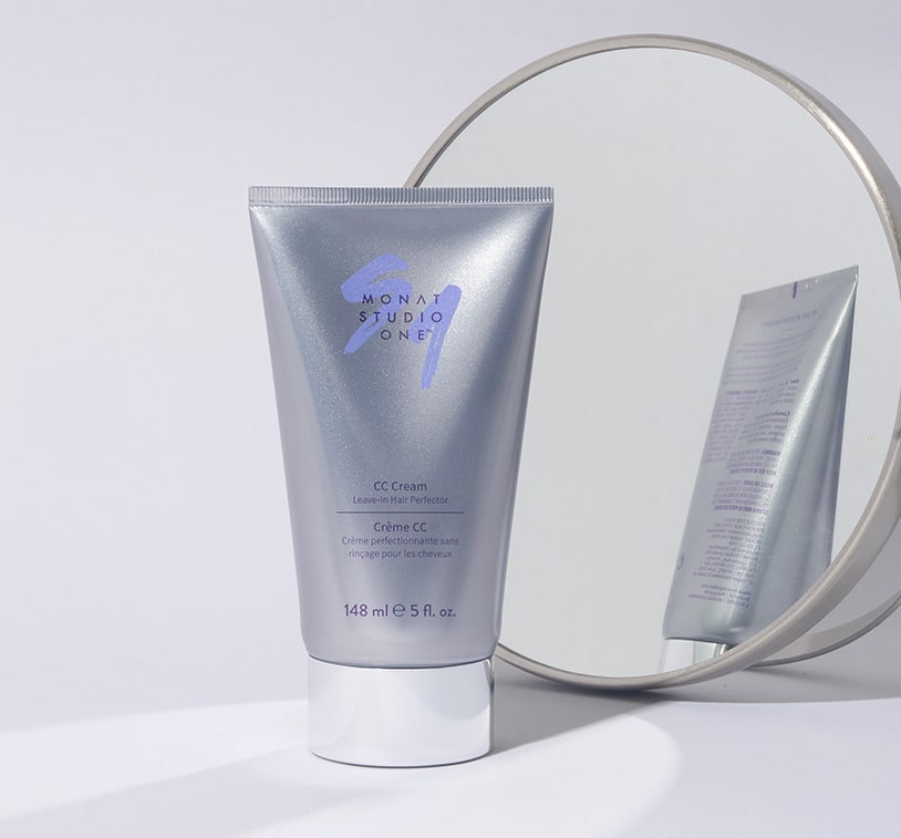 A tube of MONAT Studio One CC Cream hair product reflected in a round mirror on a white surface.