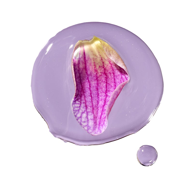  A purple flower petal resting on a smear of lavender-colored gel with a small droplet beside it.