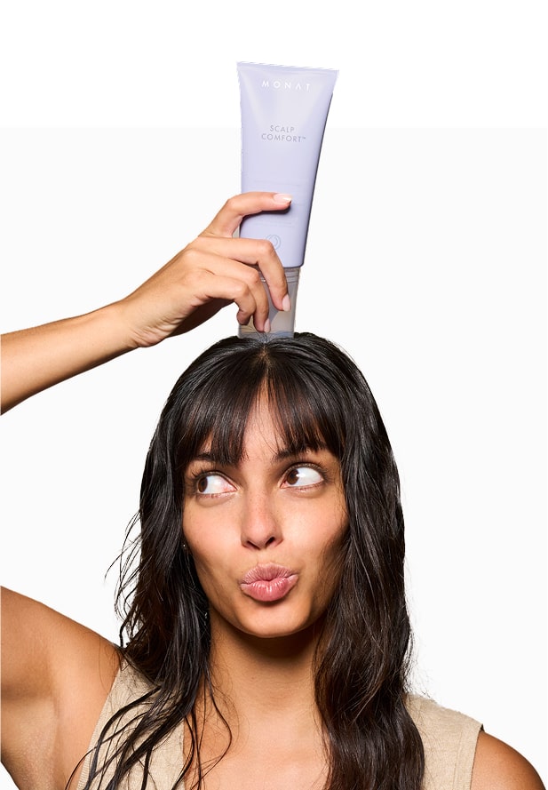 A woman lifts a MONAT scalp care product playfully, emphasizing clean beauty.