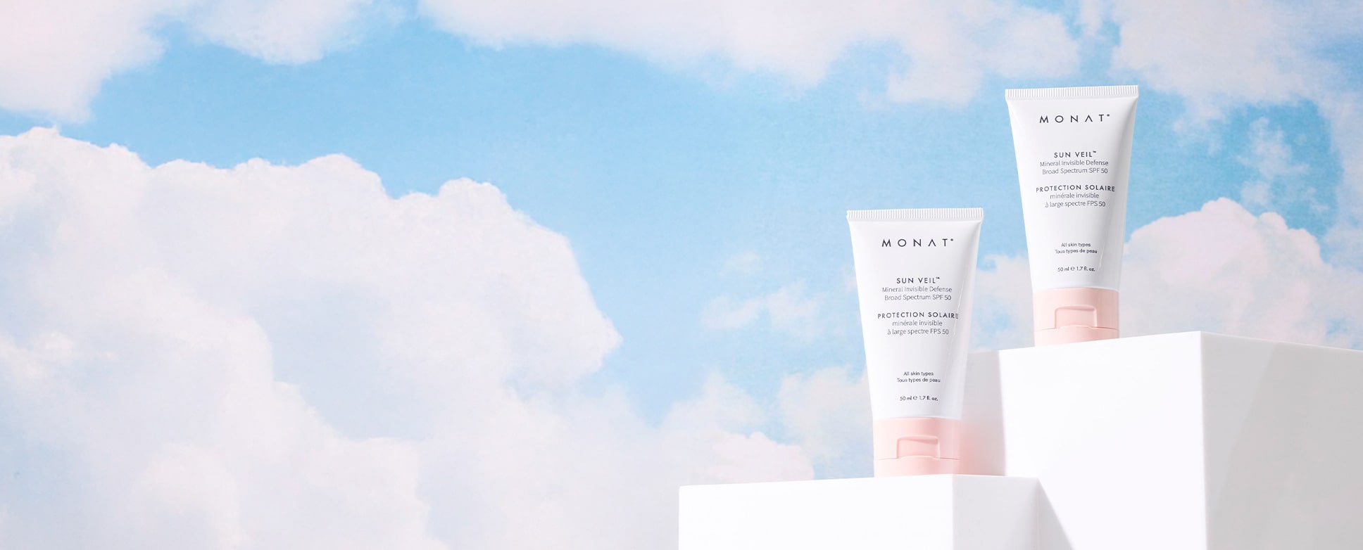 Two tubes of Sun Veil SPF 50 sunscreen on a white pedestal against a backdrop of cloudy sky.