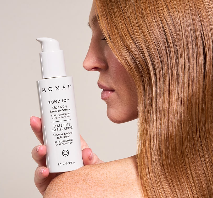 Profile view of a woman with straight, honey-blonde hair pulled back, holding a MONAT BOND IQ serum bottle