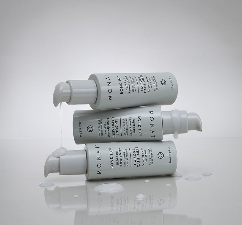 Three white MONAT BOND IQ serum bottles arranged at different angles on a reflective white surface with water droplets scattered around them
