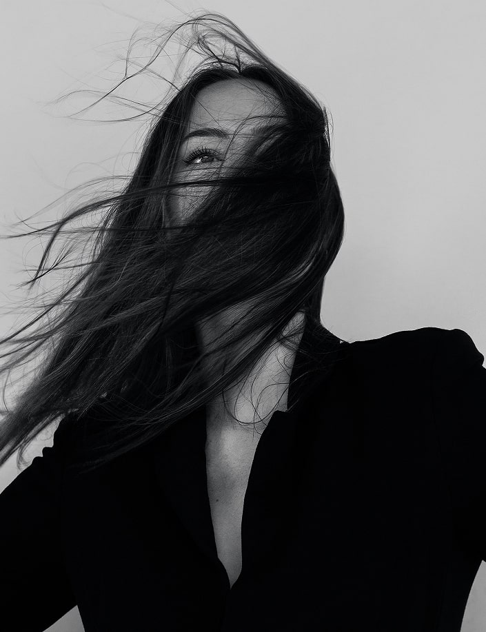 A dramatic black and white portrait of a woman with long dark hair flowing and moving in the wind