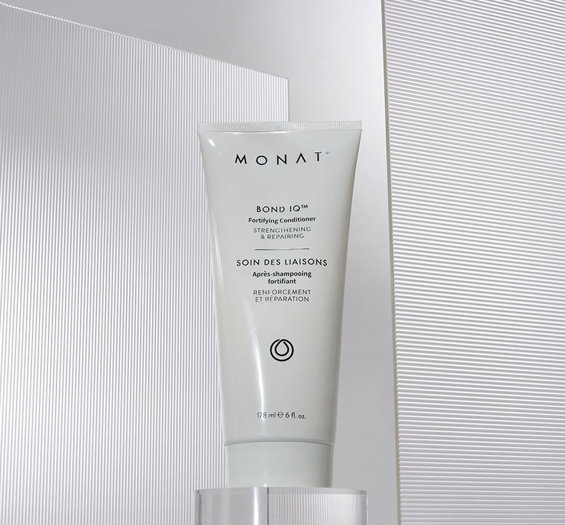 hot of a MONAT BOND IQ Fortifying Conditioner tube positioned on a clear glass platform against a white background with subtle linear textural elements